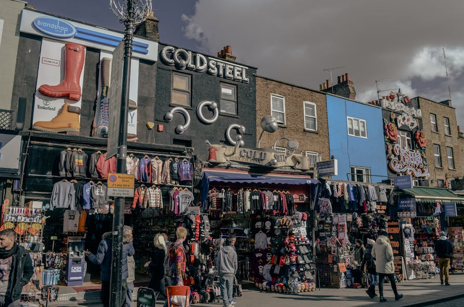The image depicts a busy street scene in Camden Town featuring a row of brick commercial buildings with colorful exteriors, including a prominent black building with the sign 'COLDSTEEL' and walls dec