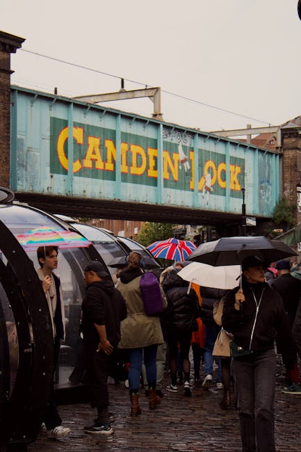 The image depicts a busy street scene in Camden Town featuring a row of brick commercial buildings with colorful exteriors, including a prominent black building with the sign 'COLDSTEEL' and walls dec